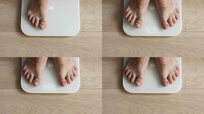 男性赤脚踩在白色数字地磅上-男人在家称自己: 特写俯视图。测量体重、技术、控制、健康和饮食概念
