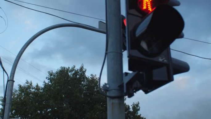 在多云的天空下，城市街道上的红绿灯特写镜头。红色变为绿色，熄灭并点亮。人行横道