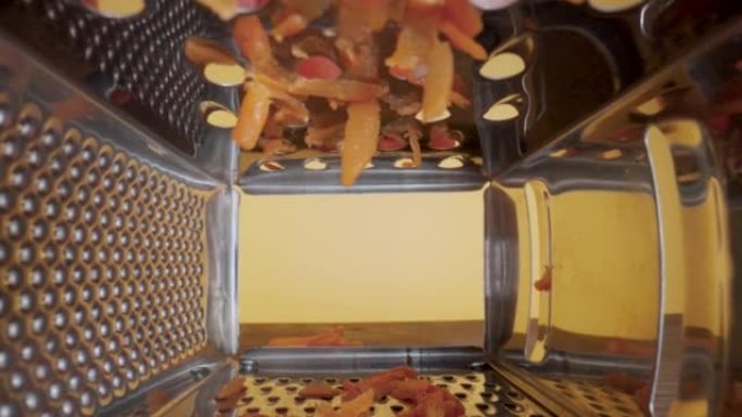 在黄色背景上的金属刨丝器光栅煮熟的胡萝卜的内部视图。磨碎机有许多用于摩擦产品的尖锐孔。不锈钢厨房工具