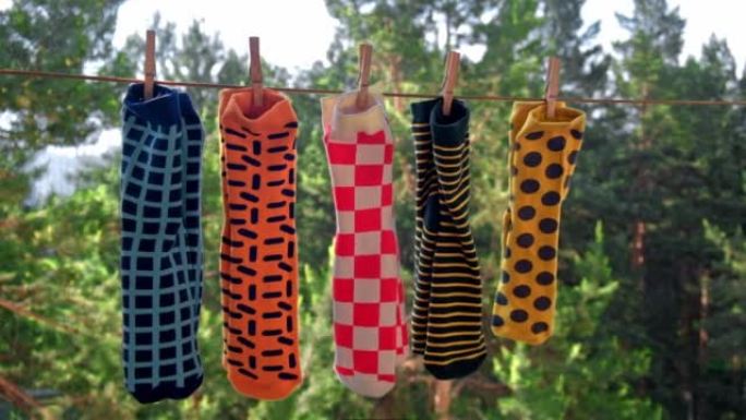 不同图案的鲜艳的男袜在一根绳子上晾干，成对地附上木制衣夹。特写。