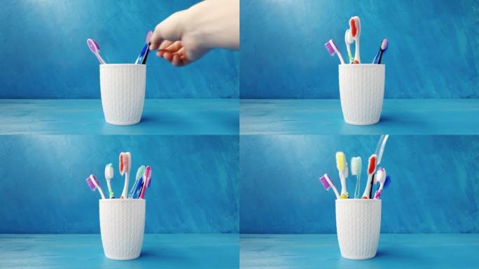 一只手将不同的多色牙刷放入蓝色背景上的杯子特写镜头中。4k原始视频。