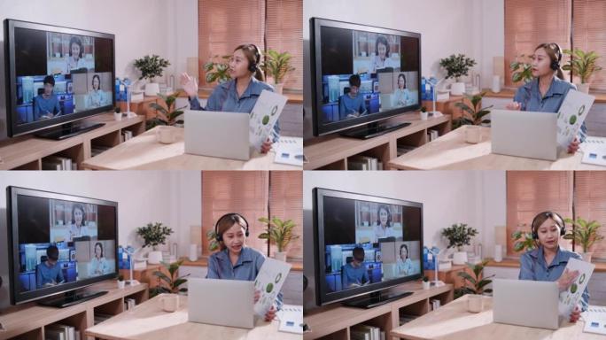 年轻的亚洲女商人戴着耳机坐在她的桌子上，用笔记本电脑和电脑屏幕在网上会议上向她的同事展示商业计划表