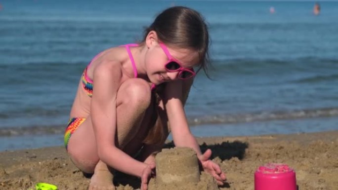 穿着泳衣的小女孩在阳光灿烂的夏日在热带海滩上建造一座沙堡