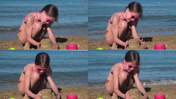 穿着泳衣的小女孩在阳光灿烂的夏日在热带海滩上建造一座沙堡