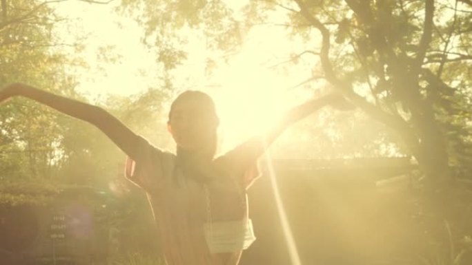 亚洲女孩举手，在户外公园的树木中晒太阳。