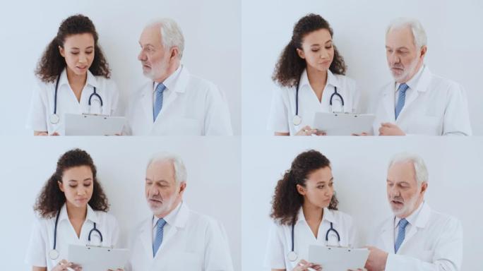 肖像两名医务人员老年白人男性和年轻卷发多种族女性，医生讨论医疗病例，在医院站在白墙边谈论健康报告