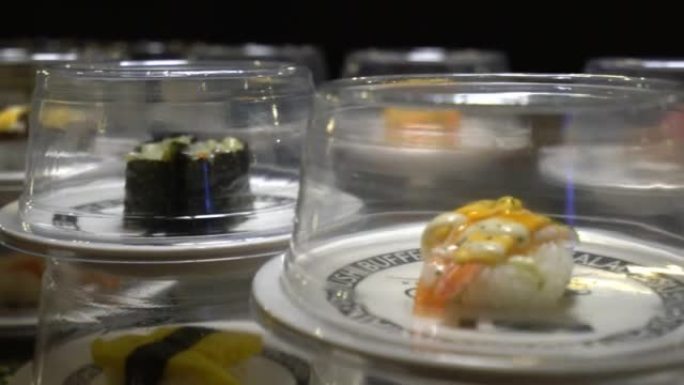 盘上不同类型的寿司和生鱼片正在寿司吧的传送带上移动