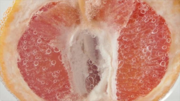 葡萄柚特写嘶嘶声或漂浮在水面。一半的粉红色葡萄柚掉入水中。