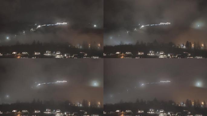 山顶上有弗洛伊巴宁缆车顶站照明建筑的浮山 -- 夜间时光倒流，雾气从挪威卑尔根山前穿过