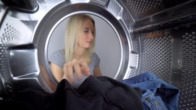 女人的手从洗衣机里取出洗过的衣服。从鼓内观看