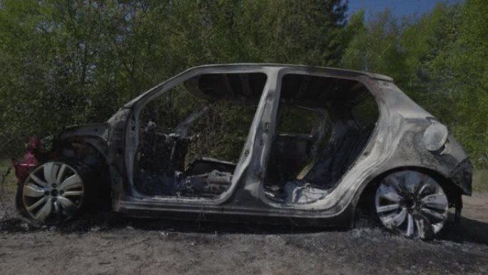 手持一张被盗汽车的照片，这辆汽车已被烧毁并倾倒在田野里。小型车标致造型无标志