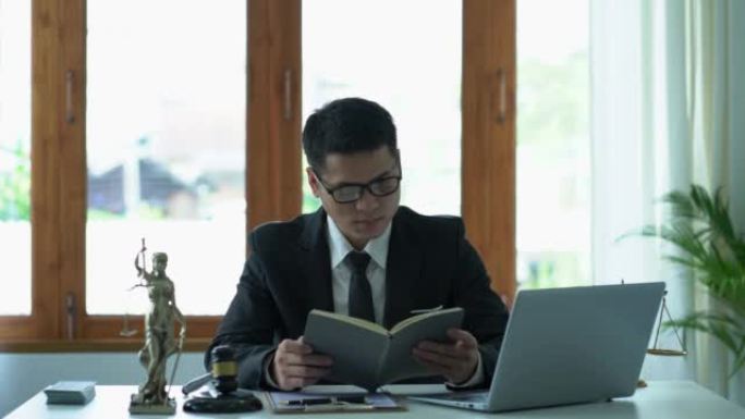 亚洲男性律师在办公室工作，在法庭桌上用木锤和女神天平与笔记本电脑。正义理念与法律良好服务咨询