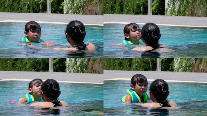 穿着救生衣的小女孩害怕在深水池里游泳。母亲教女儿在游泳池里练习游泳。幸福的家庭，母亲和女儿在游泳池里