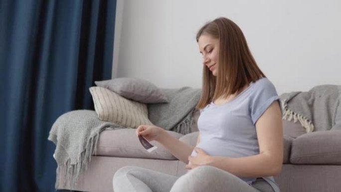 孕妇看着未出生婴儿的胎儿的第一张照片。监测怀孕的现代技术。通过超声确定孩子的性别
