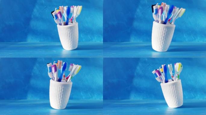 白色杯子中的许多不同牙刷在蓝色背景下在桌子上旋转。4k创意原始循环视频，具有速度斜坡效果。在高速电影