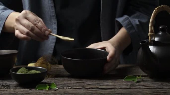 用铁丝打蛋器在木桌上的黑色碗中制备日本有机抹茶绿茶粉，天然有机产品，具有传统风格的健康