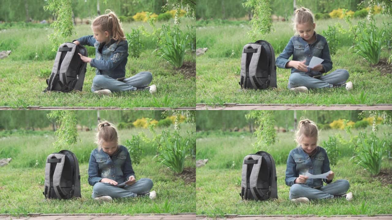 一个学龄女孩坐在草地上的公园里，仔细阅读。现代儿童的日常生活。中学教育。