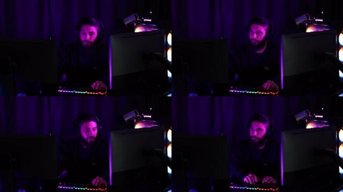 一个男人的手在带有反光耳机的黑色桌子上玩手机游戏的特写镜头。有一个装有五颜六色灯光的电脑键盘。