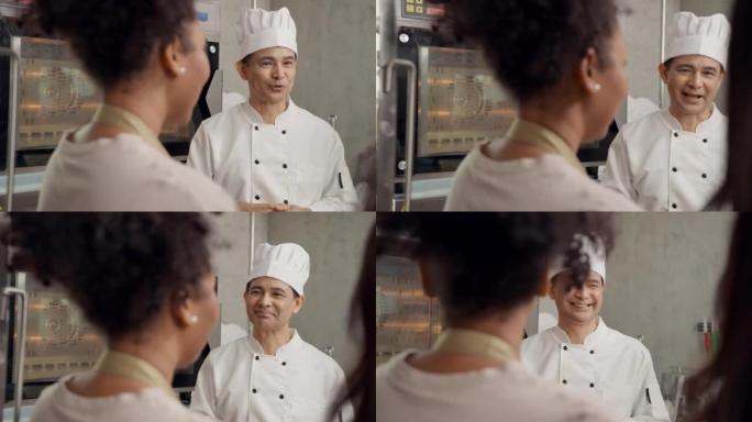 抬头看: 快乐的高级专业厨师老师在商业厨房的糕点烹饪班车间里教他的年轻成年多种族学生使用烤箱做糕点和