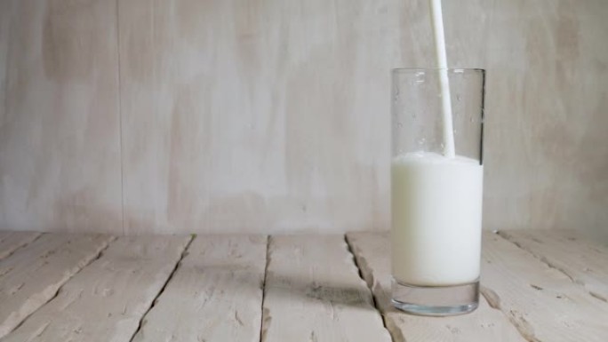 复制空间将酸奶倒入白色老式木板上的玻璃杯中。透明玻璃杯中的牛奶饮料