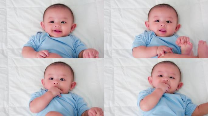 幸福的家庭，可爱的亚洲新生婴儿穿着蓝色衬衫躺在白色床上玩耍，看着相机笑着开心的脸。天真的小新婴儿可爱