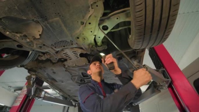 维修服务站的年轻汽车机械师检查举升汽车的车轮和悬架细节。底视图。