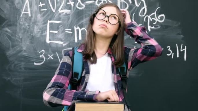 戴着眼镜和蓝色背包的少女女学生站在黑板背景上思考。然后她用手指指着，因为找到了答案。头脑风暴和明亮的