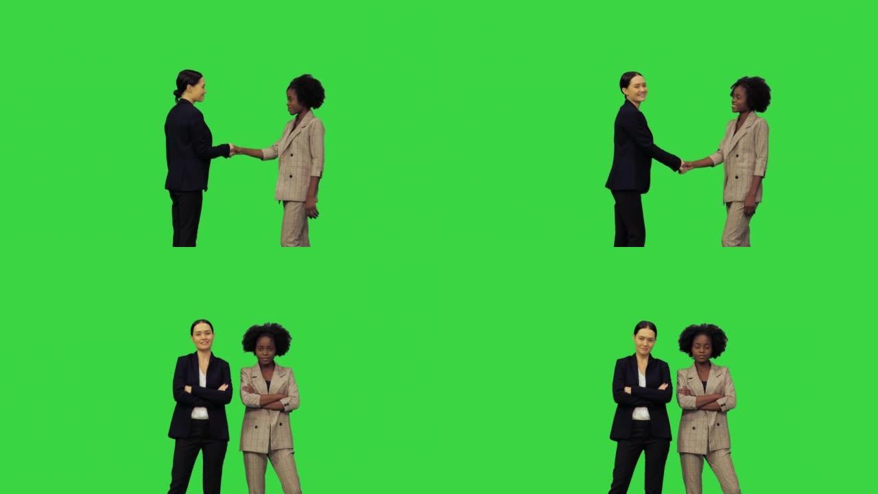 一个女孩用东西祝贺另一个女孩，并握手，然后他们转身在绿色屏幕上摆姿势拍照，色键