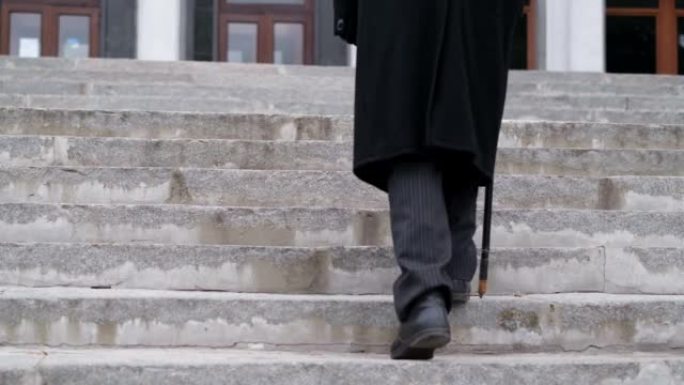 一位穿着黑色外套的老爷爷爬楼梯，步履艰难。80岁的老人