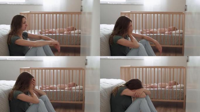 患有产后抑郁症的母亲坐在地板上，头跪在婴儿床旁边