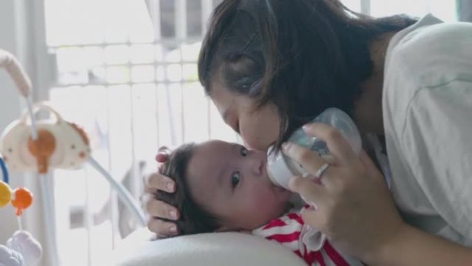 快乐的亚洲妈妈正在家里用奶瓶哺乳。