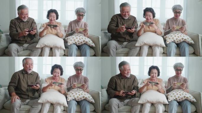 幸福亚洲退休朋友享受玩和比赛游戏智能手机在线沙发在客厅家庭室内背景，亚洲团体一起玩游戏家庭孤立的想法