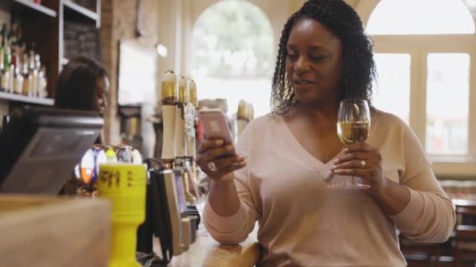 女人喝白葡萄酒并在酒吧使用智能手机