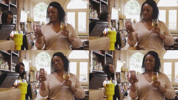 女人喝白葡萄酒并在酒吧使用智能手机