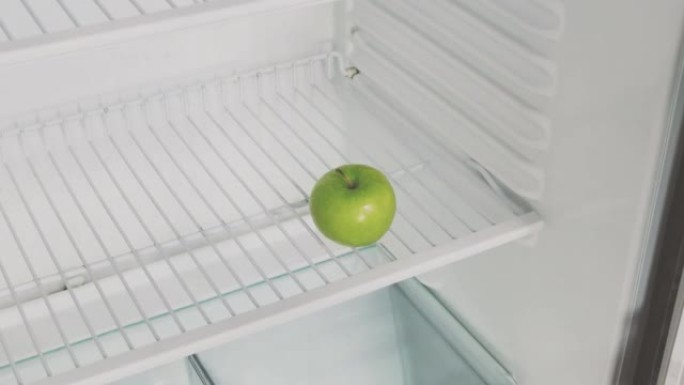 这个人的手打开一个空的冰箱，上面放着危机这个词，然后拿了一个绿色的苹果。概念性4k原始视频。经济危机