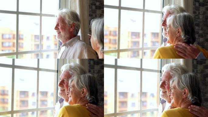 幸福的恋爱中老年退休夫妇站在窗户旁，望着远方，回忆美好的回忆或规划共同的未来，一起在家享受和平的时刻