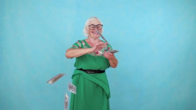 快乐积极的老年妇女在蓝色背景上扔纸钞