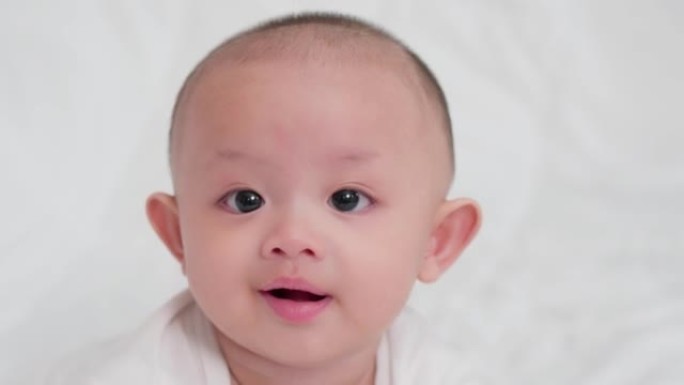真实拍摄的肖像脸可爱的亚洲新生婴儿，同时在白色床上玩耍，看着相机笑着开心的脸。天真的小新婴儿可爱。父