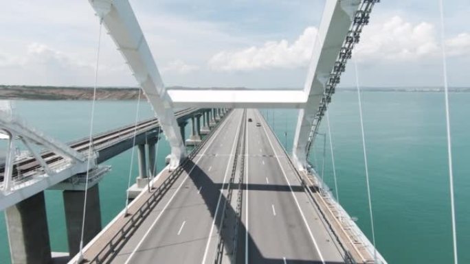 巨大的桥梁。无人机视图。行动。一座横跨海洋的长桥，汽车可以在上面自由移动，这座桥位于绿色的山脉旁边