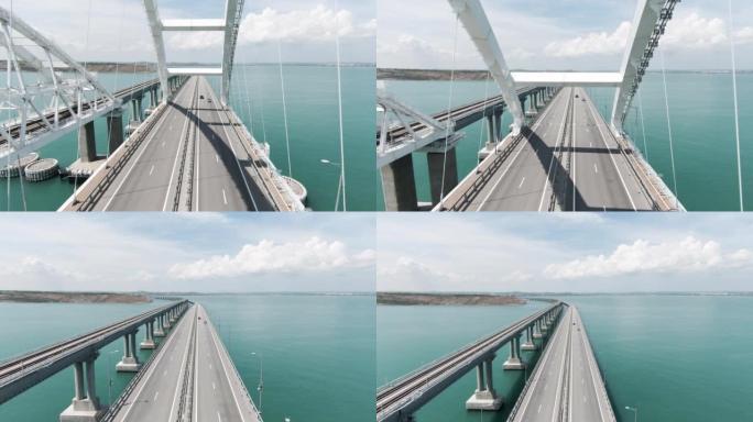 巨大的桥梁。无人机视图。行动。一座横跨海洋的长桥，汽车可以在上面自由移动，这座桥位于绿色的山脉旁边