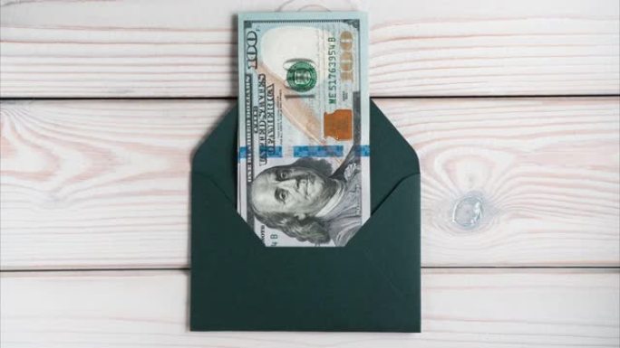 封闭的绿色信封出现在灰色的木桌上，打开。从信封中散开的百元钞票。