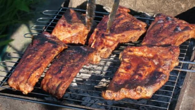 火烧烤架上的烤排骨。夏天晚上，人们在明火上烧烤排骨。美食户外午餐街头美食慢动作特写