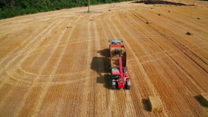 农用挖掘机将干草捆放入拖拉机中。采摘麦收后在地里工作的机械。