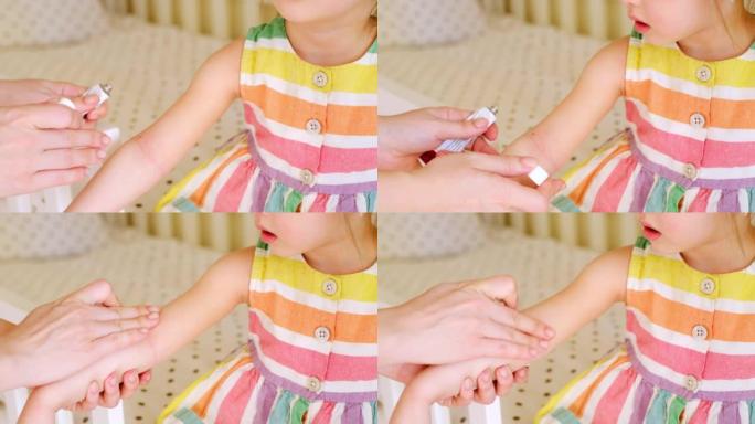妇女将乳霜从管到患有特应性皮炎的儿童的不健康，疾病皮肤。婴儿手臂弯曲处的红色粗糙斑点。用于缓解过敏性