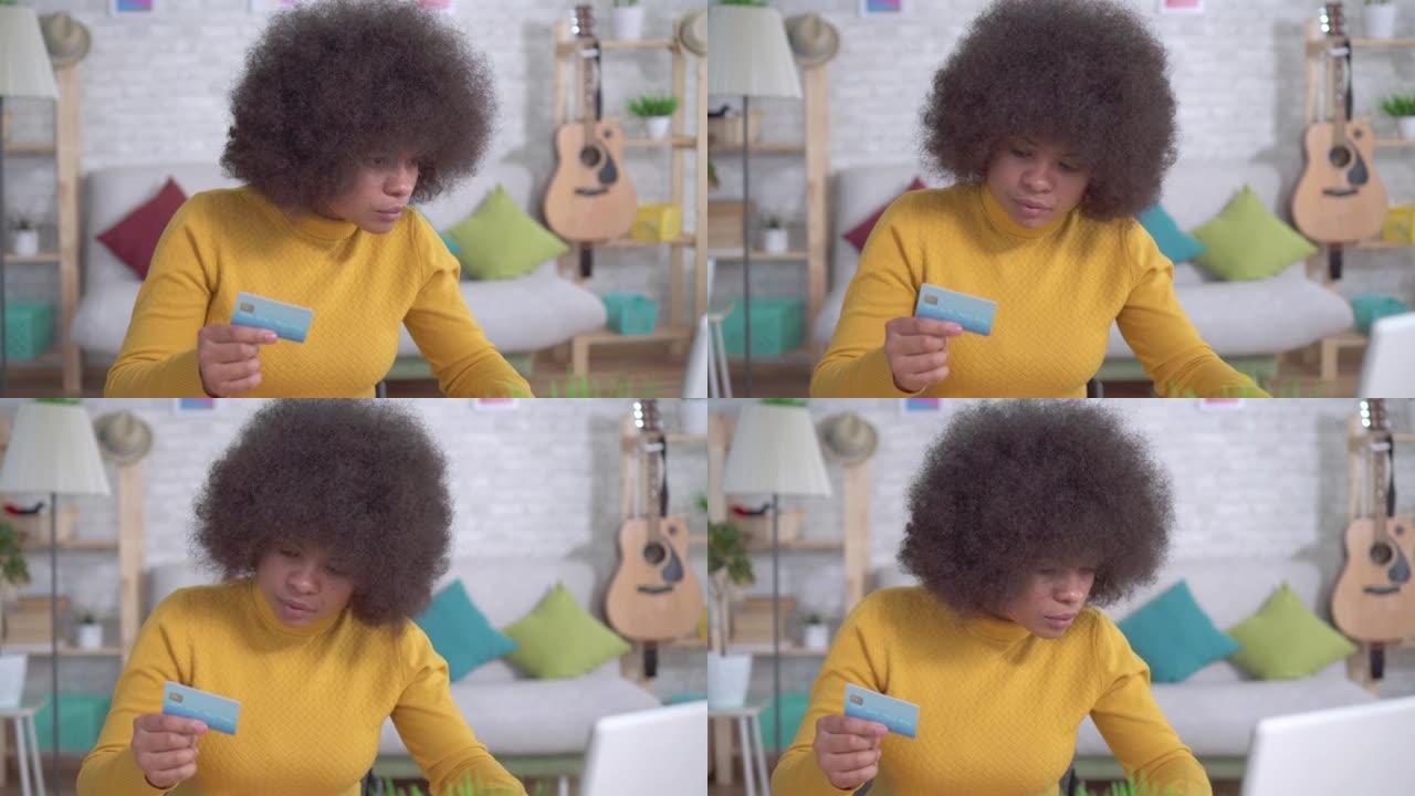 美丽的非洲裔美国女孩，非洲发型，手里拿着银行卡，现代公寓里有一台笔记本电脑特写