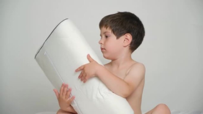 一个5岁的男孩坐在床上时抱着他最喜欢的矫形枕头。