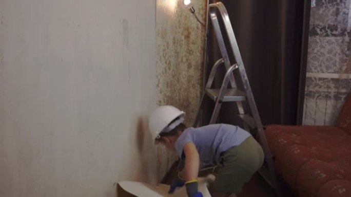 5岁的男孩从墙上撕下旧墙纸，帮助他的父亲
