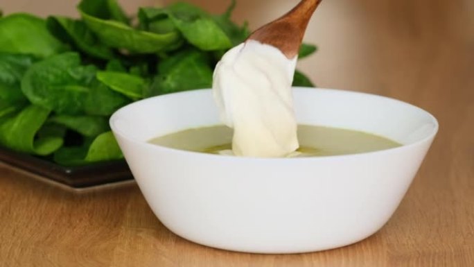 一碗健康的绿色菠菜汤配奶油。厨师用奶油装饰菠菜或西兰花汤。菠菜奶油汤。在汤特写中加入酸奶油