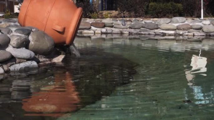 水从一个大的棕色陶罐倒入游泳池。