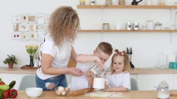 当他和他的母亲和妹妹在厨房里把面团滚出时，男孩把面粉倒入筛子里。一个穿着白色t恤的金发女郎家庭